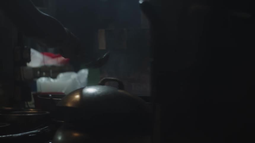 Close up of a young man adding and stirring food in a pan with a utensil while cooking in a kitchen at night