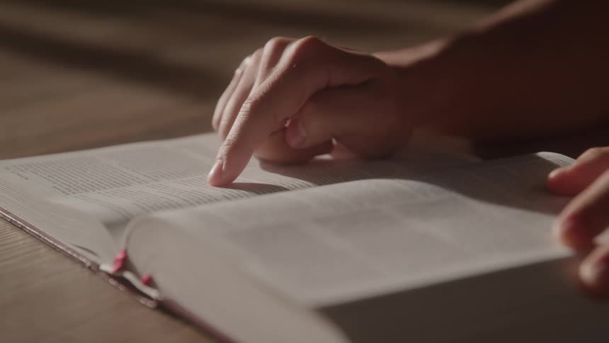 A person reads from a book and uses their finger to help guide their reading