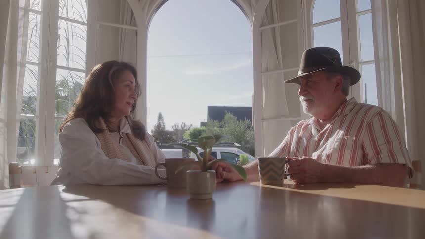 A middle aged couple sitting together while holding hands at a table indoors during daytime