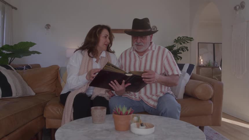 Elderly couple sitting on a sofa in the living room looking at a photo album