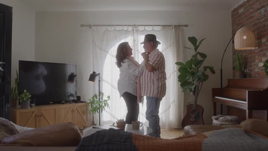 An older couple slow dancing in living room front of large window
