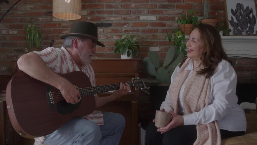 Man playing guitar while a woman sitting in front of him smiles holding a mug