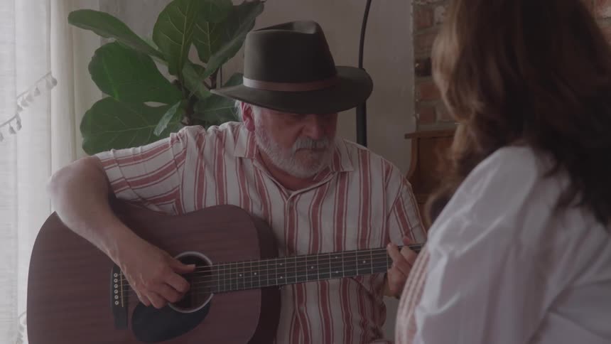 Man wearing a hat playing guitar while talking to a woman
