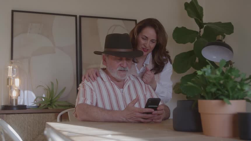 Mature couple sitting at a table looking together at a cellphone with an attentive expression