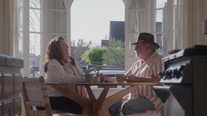 Couple sitting at a table in a sunlit kitchen talking and having coffee