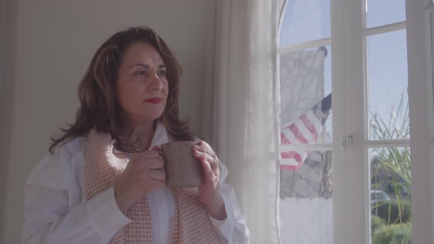 Woman holding coffee mug standing indoors looking out window