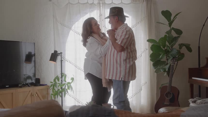 Older couple slow dancing in living room front of large window