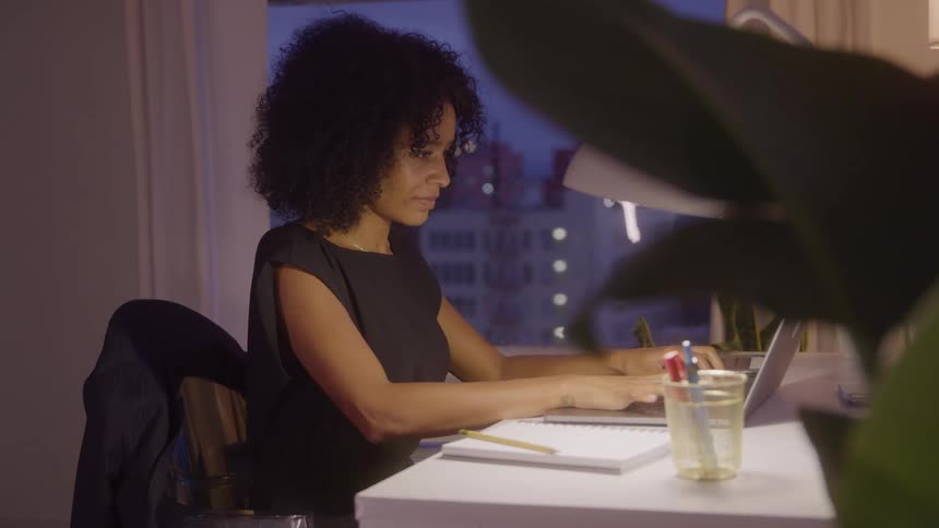 Woman working on a laptop at night in a welllit modern space
