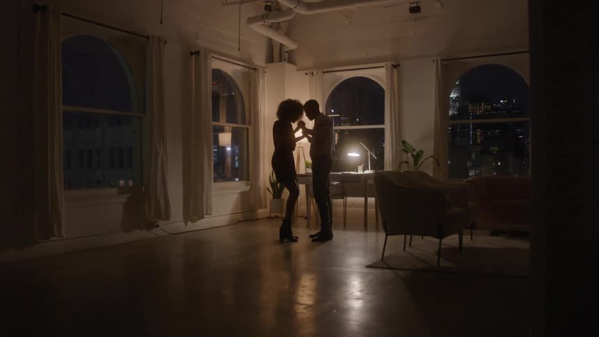 Couple dancing intimately in a loft lit by the city at night