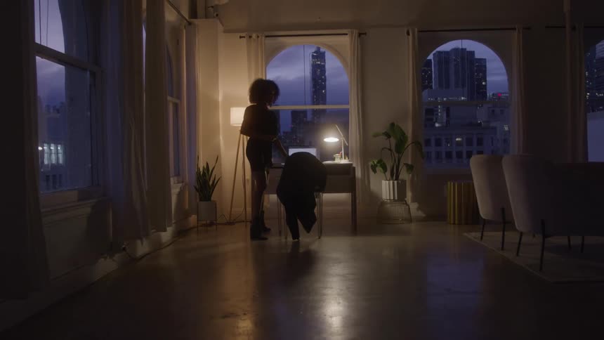 A woman stands up from a desk and walks away through an apartment