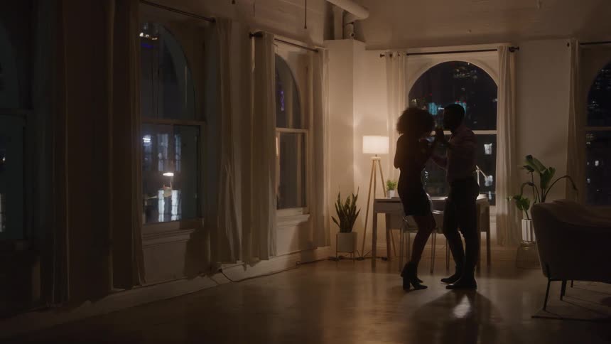 Couple dancing in a spacious room with windows lit by the city at night
