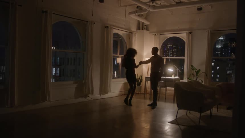 A young black adult couple dancing together in a living room at night