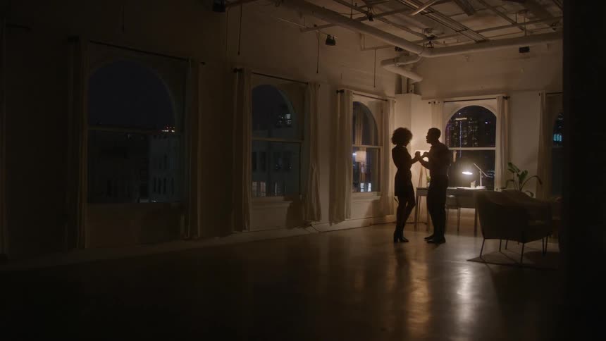 A young black adult couple dancing together in a room at night