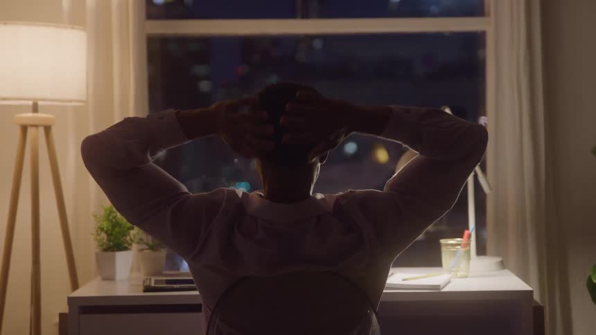 Close up of a young black man stretching while sitting at a table indoors at night
