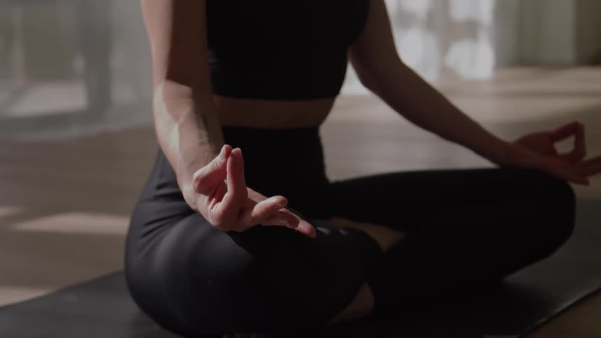 A woman in gym clothes sitting in the lotus position on a yoga mat meditating