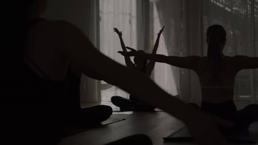 Yoga instructor leads a class in a heavily curtained room during the daytime