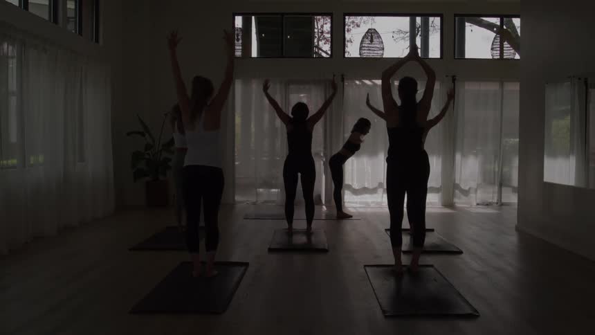 People practice yoga with raised arms in a bright studio