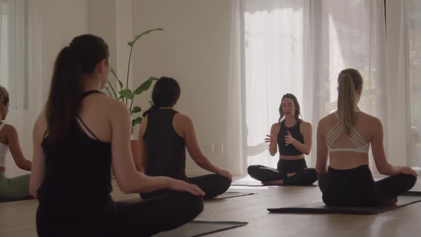A group of women sit on mats while practicing yoga with an instructor