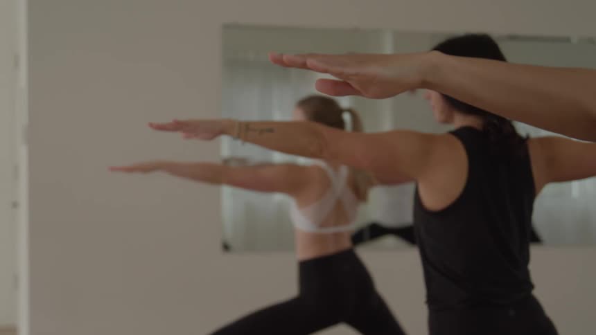 Practitioners perform warrior pose with arms extended during a yoga class