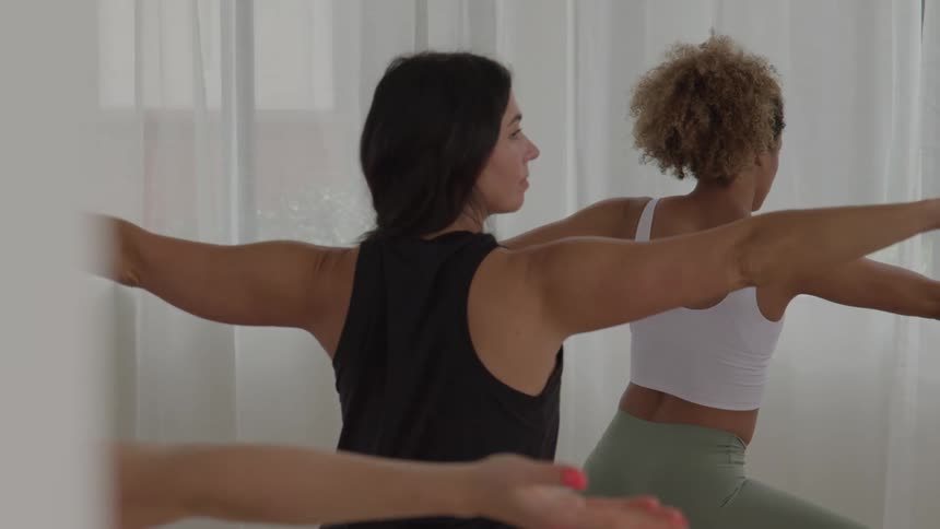 Women practice yoga in a balancing pose with arms extended