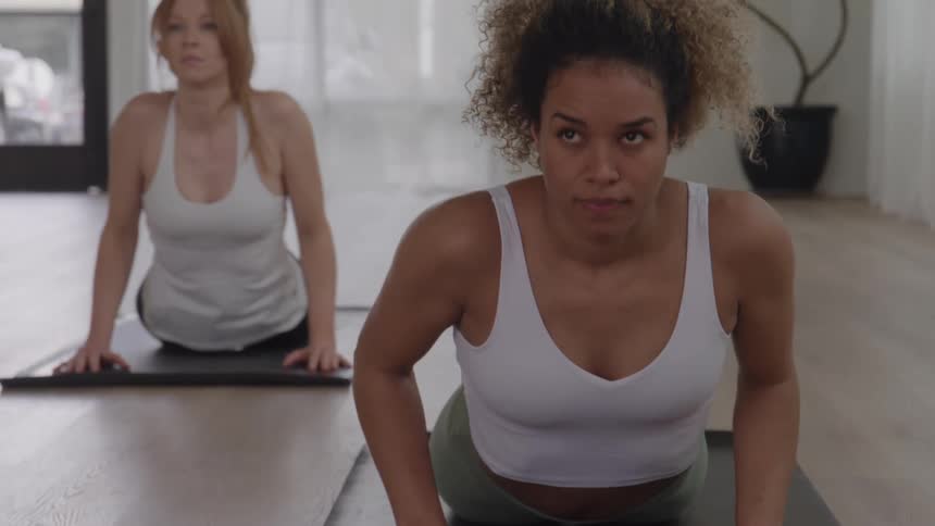 Women move through yoga poses in unison while working out inside during the daytime