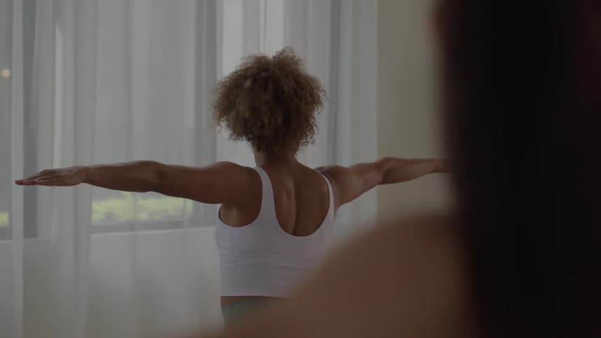 Women stand in a yoga pose while in a curtained room