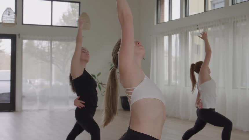 Women in a daytime yoga class move through multiple poses