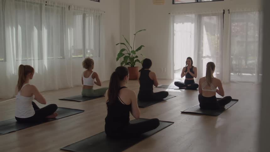 Several women sit on mats while practicing yoga with an instructor