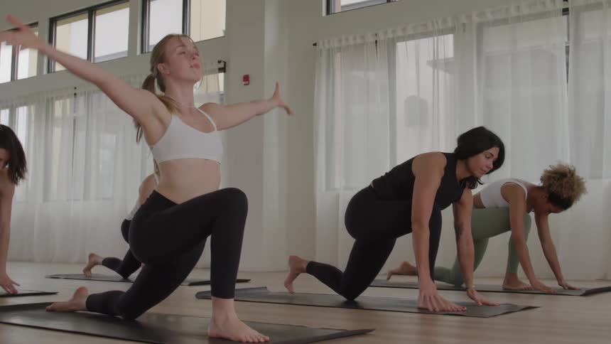 A group of young women stretching while performing yoga in a room during daytime