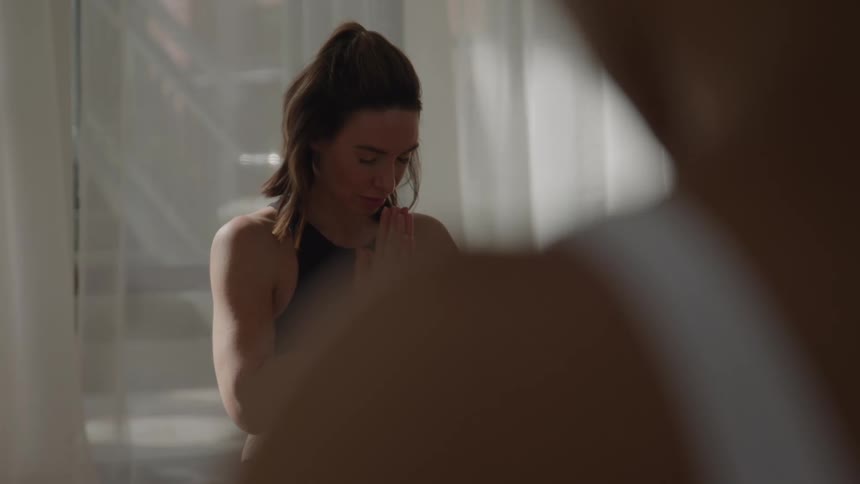 The video shows a woman with her hair pulled up in a ponytail sitting and engaging in a moment of mindfulness or meditationshe slowly brings her hands up to her chest in prayer position anjali mudra holding a serene and focused expressio