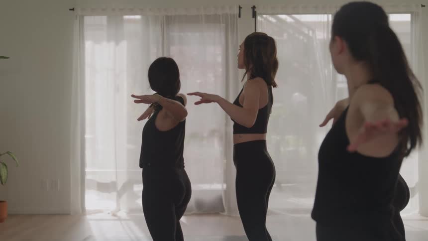 Female instructor guides her students through a yoga pose in a yoga studio