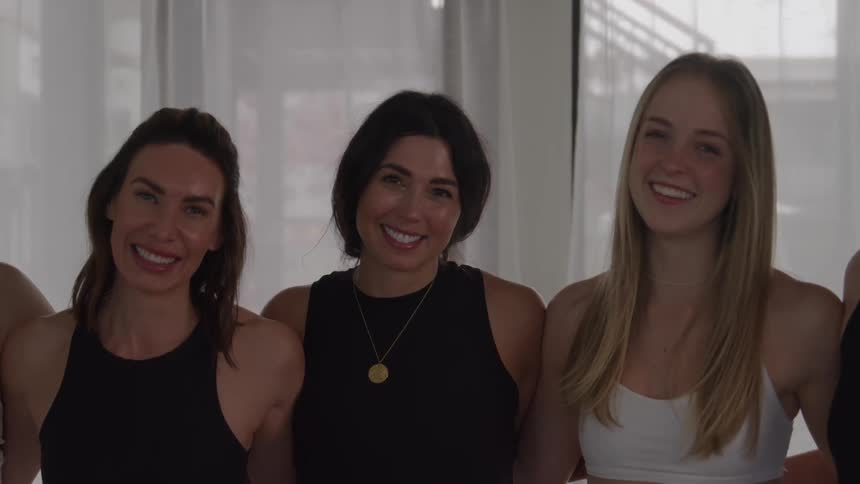 Three smiling women in athletic wear looking directly at the camera in a bright studio