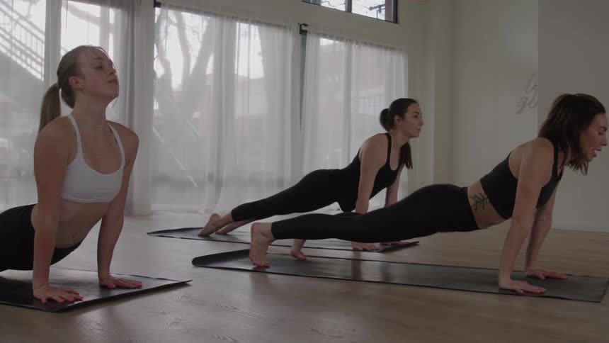 Three young women stretch indoors at midday each on her own yoga mat