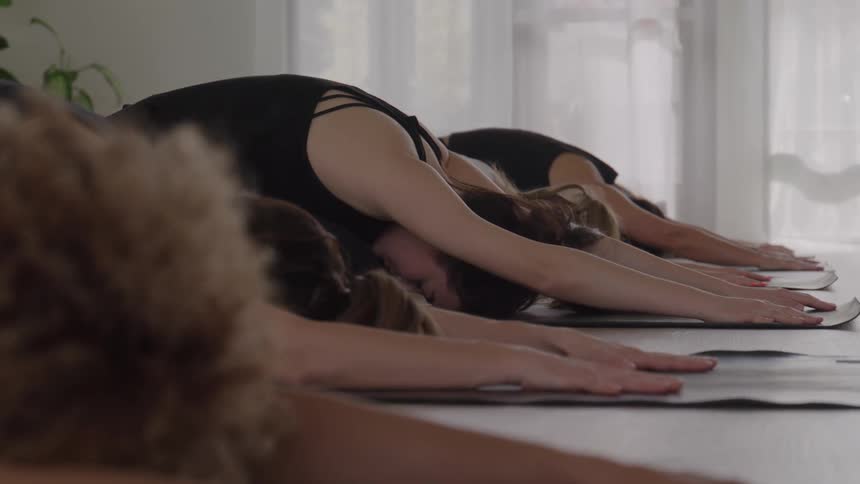 A group of women stretches indoors at midday holding a yoga pose while wearing black tops