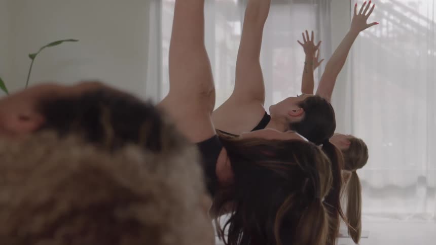 The video captures a group of women in a bright studio holding an intense inversion or corestrengthening yoga posethe women are on their backs with their legs and arms extended straight up toward the ceiling creating a strong dynamic line wi