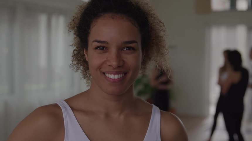 Woman standing in a yoga class faces forward while smiling broadly