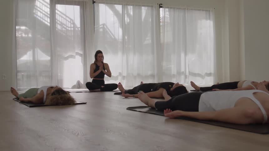 Practitioners lie in savasana while the instructor remains seated at the front