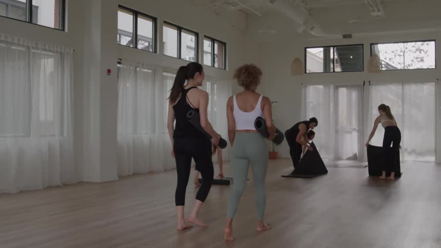 The women talk and lay out mats in the yoga studio