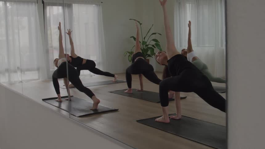Practitioners perform a twist with one arm raised during a yoga class in front of the mirror