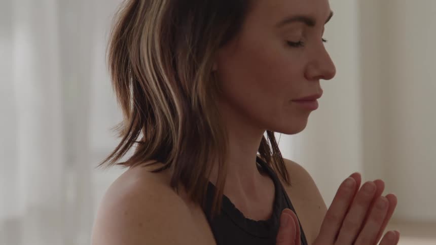 Woman keeps her eyes closed with hands joined in front of her chest