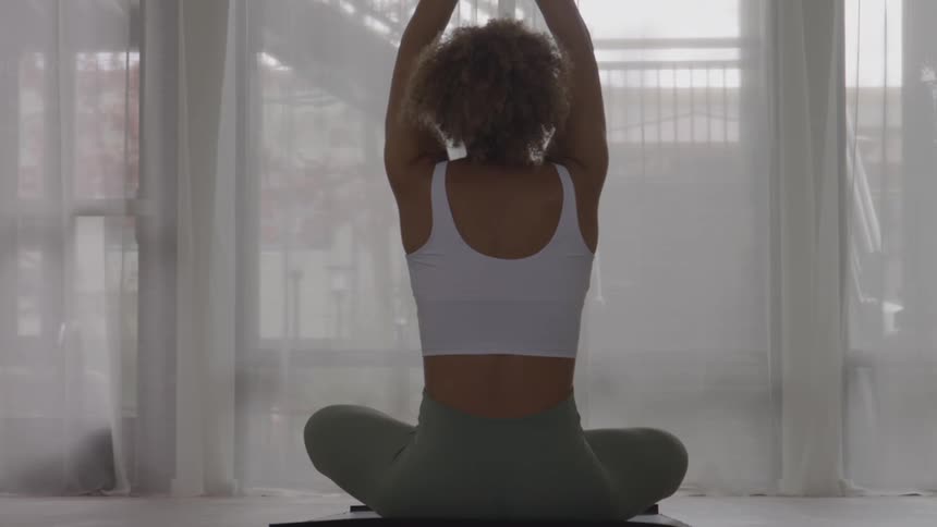 The woman stretches her arms straight up in the gym
