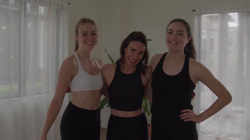 Three women pose side by side in a yoga studio