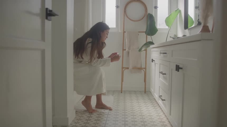Woman sits in the bathroom wearing a white robe and looks at a pregnancy test in her hands
