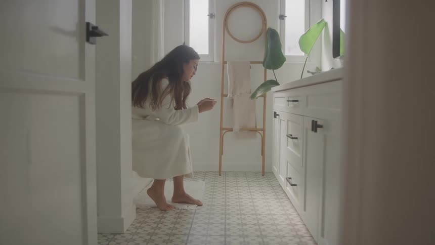Woman sits in the bathroom wearing a white robe and holding an object in her hands