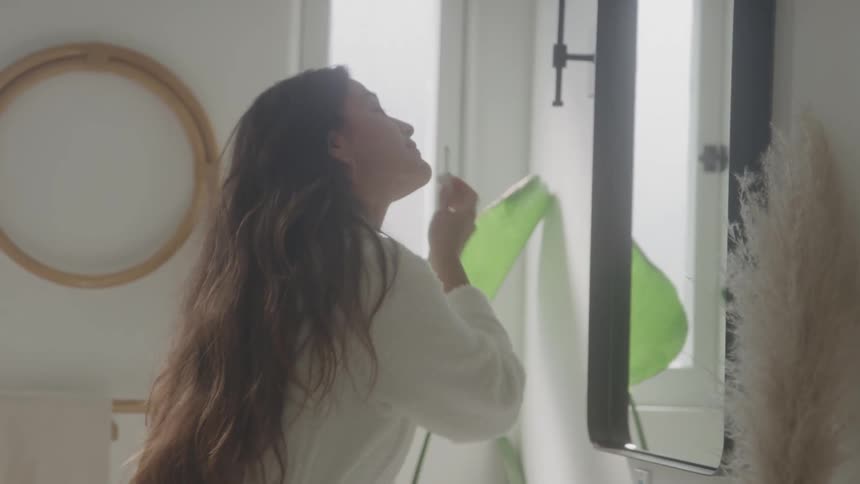 Woman applies makeup in front of the mirror wearing a white robe