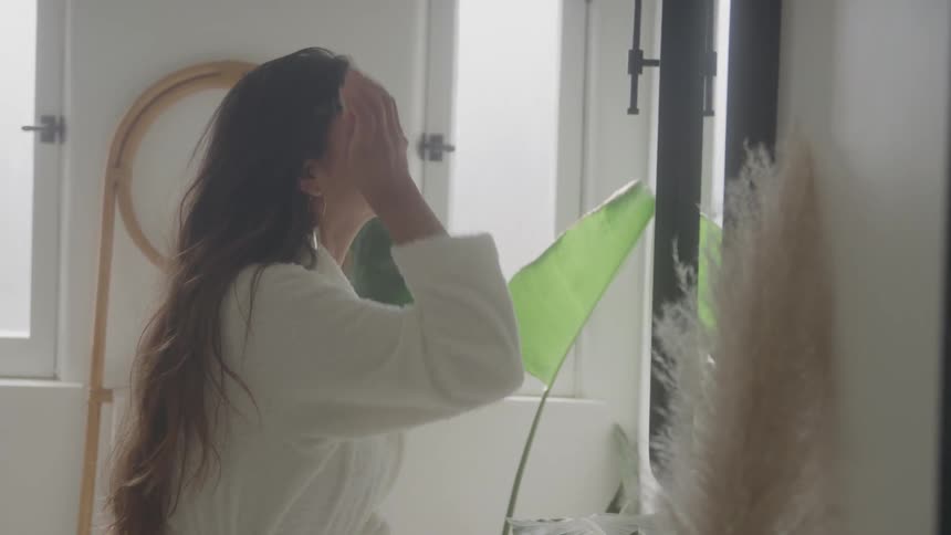 Woman applies makeup in front of the mirror wearing a white robe