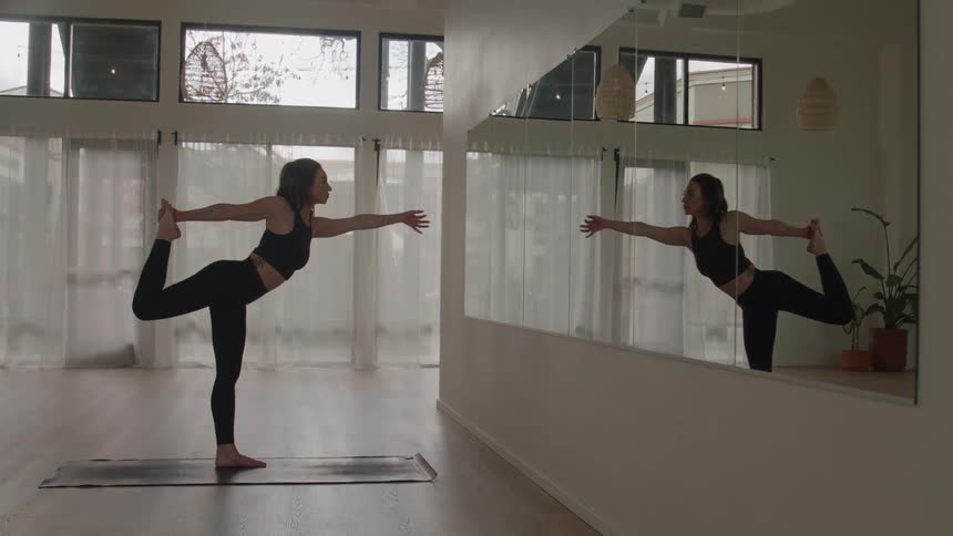 Woman practices an advanced balancing pose in a yoga class in front of the mirror