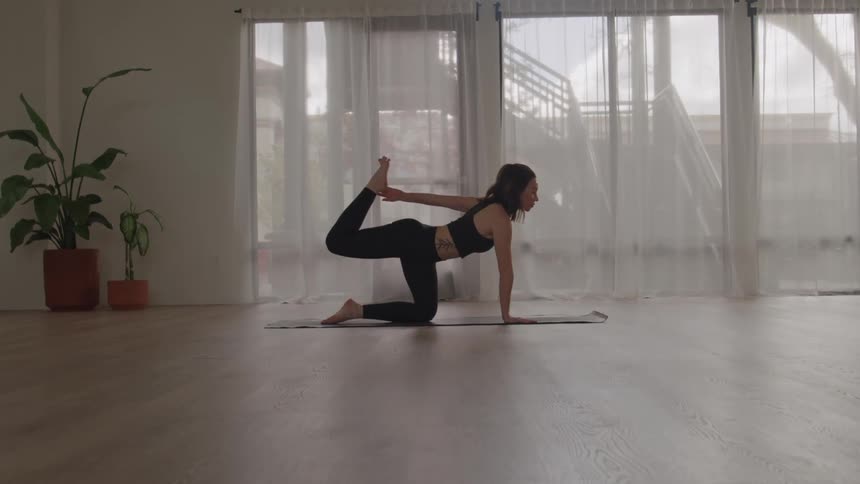 A young woman practices yoga at midday on a mat in an empty room