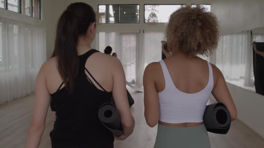 Two women walk side by side carrying rolledup yoga mats