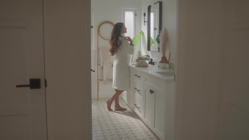 The woman is fixing her hair in the bathroom